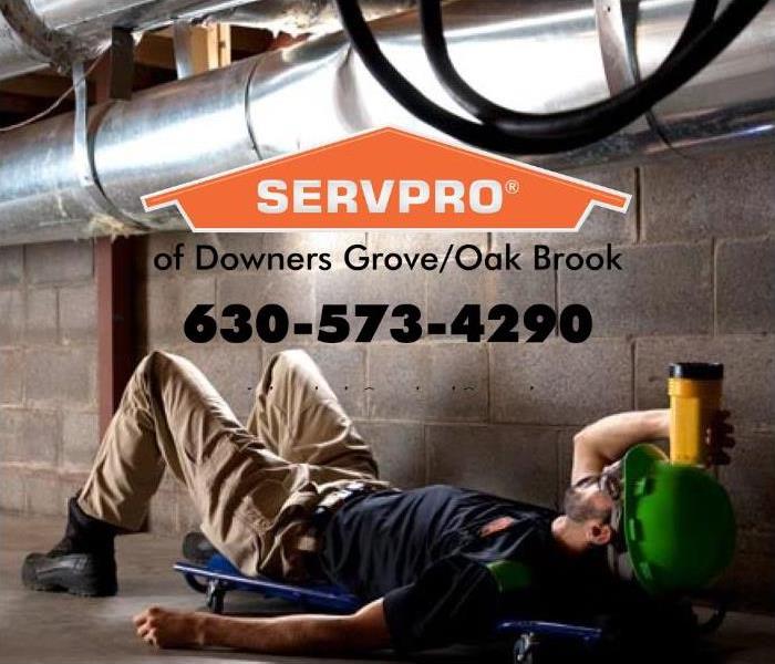 SERVPRO employee laying down with a yellow flashlight looking at a silver furnace pipe.