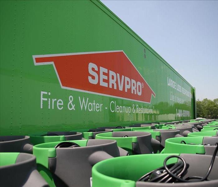 Big green SERVPRO truck with several green air movers in front of the truck.