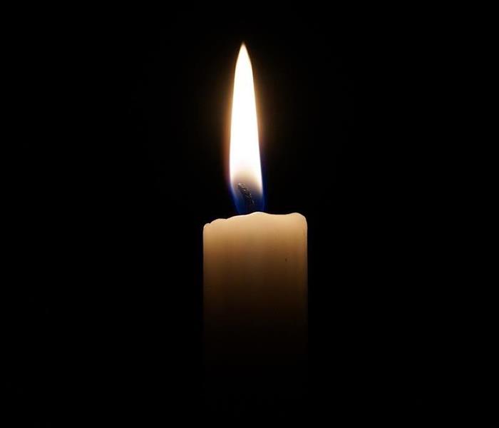 White candle with a flame with a black background.