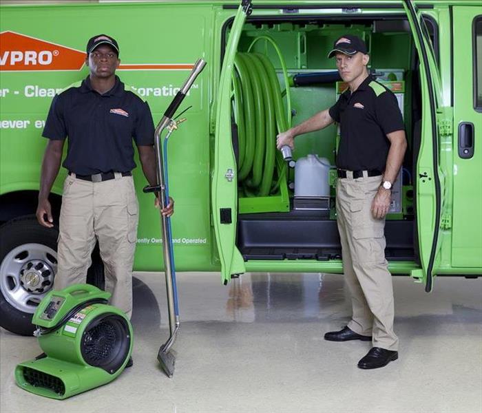 Two SERVPRO employees standing outside a van with an air mover on the ground.