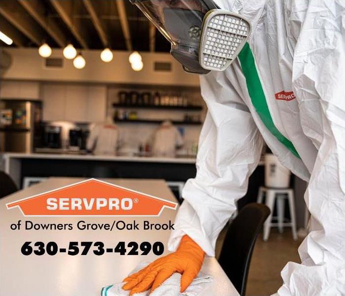 SERVPRO employee wearing PPE and wiping a table.